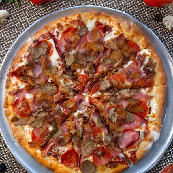 A large, uncut Uncle Ernie's pizza with pepperoni, ham, and sausage on a metal pan.