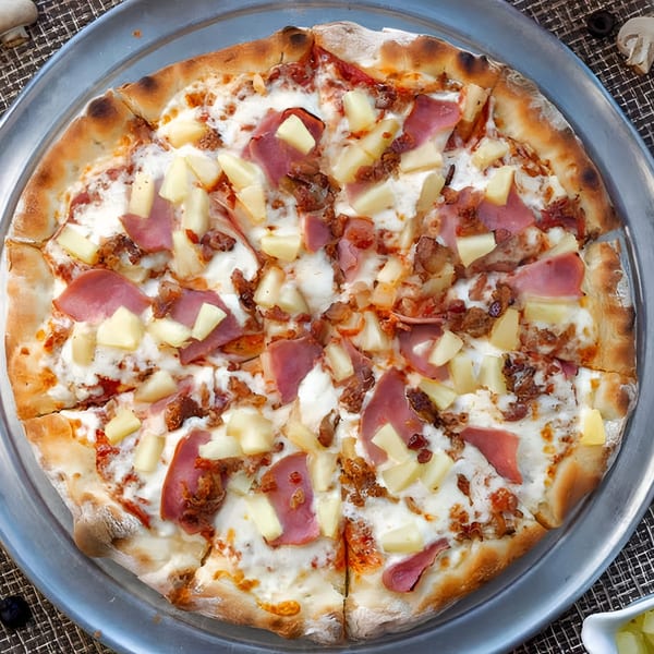 A whole Uncle Ernie's Pizza with ham, pineapple, and bacon on a metal tray.