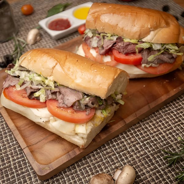 Two hearty roast beef subs with lettuce, tomato, and cheese on a wooden board.