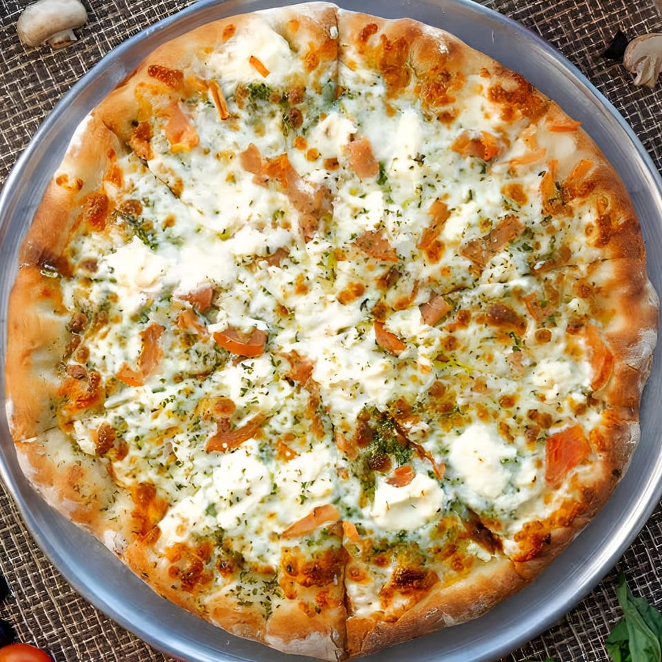 A white pizza with pesto, ricotta cheese, and sun-dried tomatoes on a metal tray.
